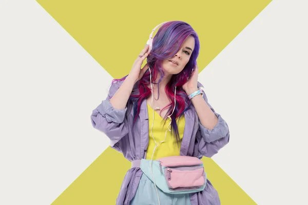 Mujer joven de moda con pelo colorido en abrigo de trinchera púrpura escuchando música con auriculares - foto de stock