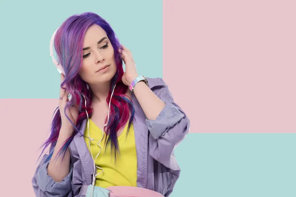 Hermosa mujer joven con el pelo colorido en gabardina púrpura escuchar música con auriculares - foto de stock