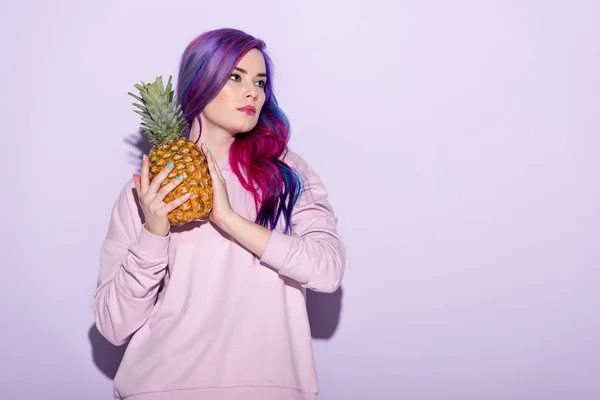 Hermosa mujer joven con pelo colorido y sudadera rosa sosteniendo piña - foto de stock