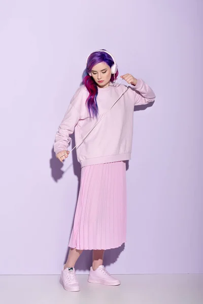 Mujer joven bailando con el pelo morado en ropa rosa escuchando música con auriculares con cable - foto de stock