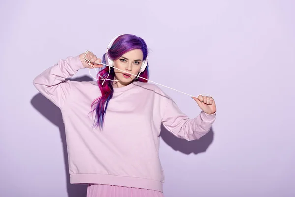 Hermosa mujer joven en ropa rosa escuchando música con auriculares con cable - foto de stock