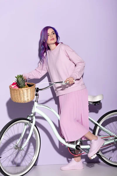 Attractive woman in pink clothing on bicycle with pineapple and bananas in basket — Stock Photo