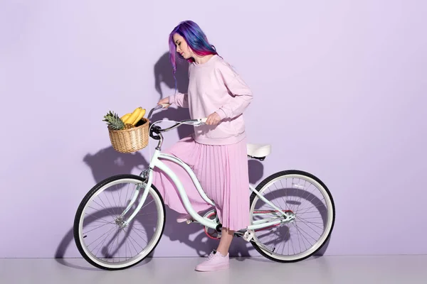 Attractive young woman in pink clothing on bicycle with pineapple and bananas in basket — Stock Photo