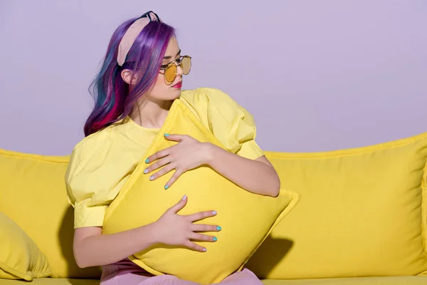 Красива молода жінка сидить на жовтому дивані і приймає подушку — стокове фото