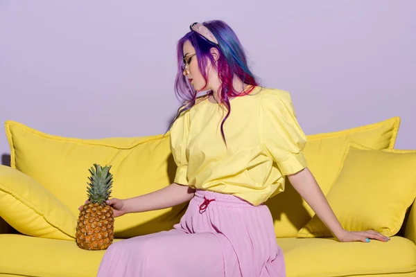 Belle jeune femme assise sur un canapé jaune avec ananas — Photo de stock