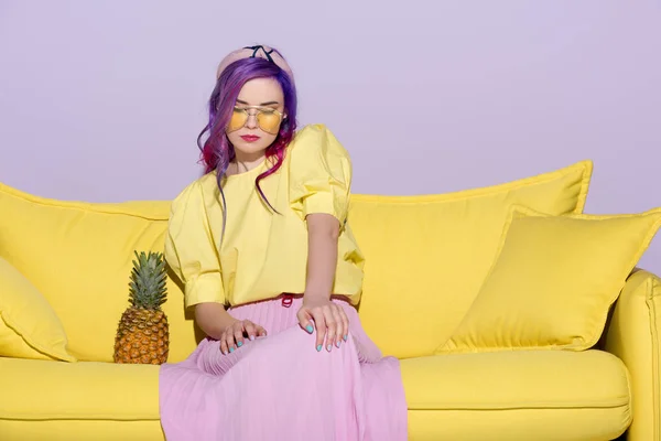 Giovane donna alla moda seduta sul divano giallo con ananas — Foto stock