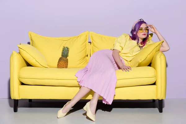 Élégante femme réfléchie assise sur un canapé jaune avec ananas — Photo de stock