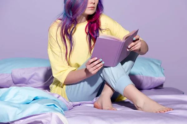 Cropped shot of young woman with colorful hair reading book in bed — Stock Photo