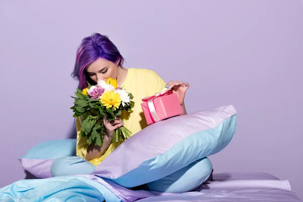 Schöne junge Frau mit Geschenkbox und Blumen im Bett sitzend — Stockfoto