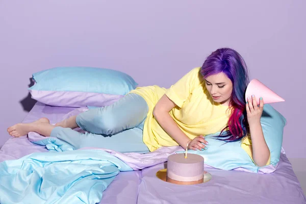 Hermosa joven con pastel de cumpleaños y sombrero de fiesta en la cama - foto de stock