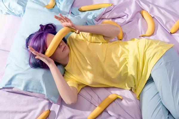 Vista de ángulo alto de la mujer joven acostada en la cama con plátanos y cubierta de la cara - foto de stock