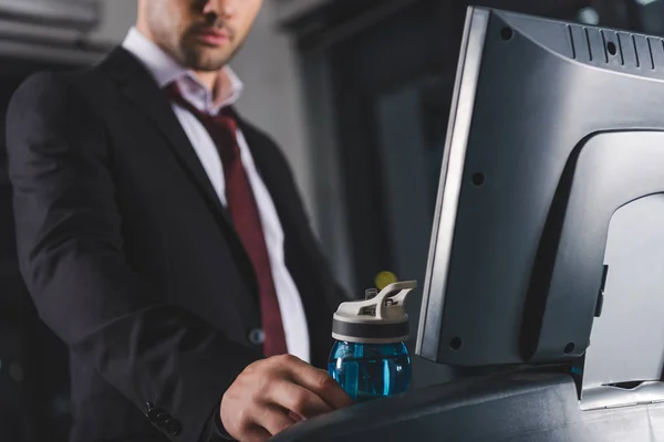 Cropped view of businessman training on treadmill and taking sport bottle in gym — Stock Photo