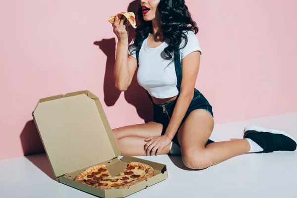 Частичный вид молодой женщины, которая ест пиццу на розовом фоне — стоковое фото