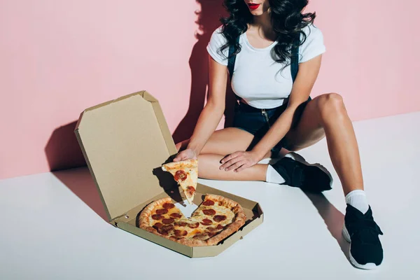 Partial view of stylish woman and delivery box with pizza on floor on pink backdrop — Stock Photo