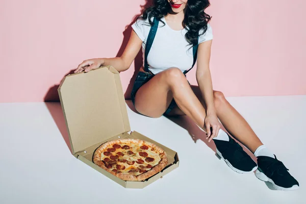 Partial view of stylish woman and delivery box with pizza on floor on pink backdrop — Stock Photo