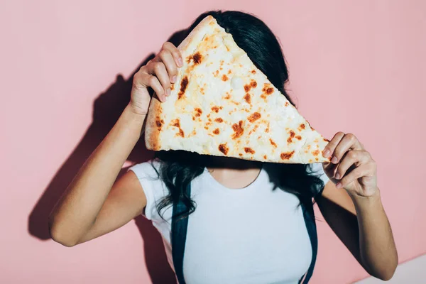 Verdunkelte Ansicht einer Frau, die ihr Gesicht mit einem Stück Pizza auf rosa Hintergrund bedeckt — Stockfoto