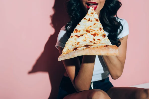 Частичный вид женщины, которая ест пиццу на розовом фоне — стоковое фото