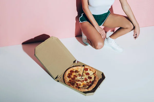 Частковий вид на стильну жінку і коробку доставки з піцою на підлозі на рожевому тлі — стокове фото