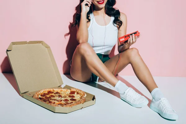 Cropped shot of smiling woman with retro music player and delivery box with pizza on pink background — Stock Photo