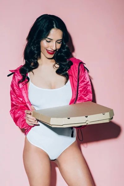 Smiling woman in white bodysuit holding delivery box with pizza on pink backdrop — Stock Photo