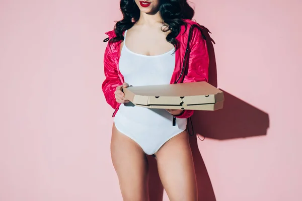 Partial view of woman in white bodysuit holding delivery box with pizza on pink backdrop — Stock Photo