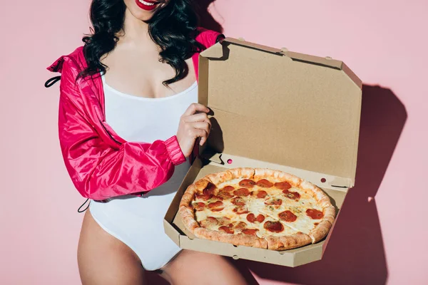 Tiro recortado de la mujer en el bodysuit blanco que sostiene la caja de entrega con la pizza en el telón de fondo rosa - foto de stock