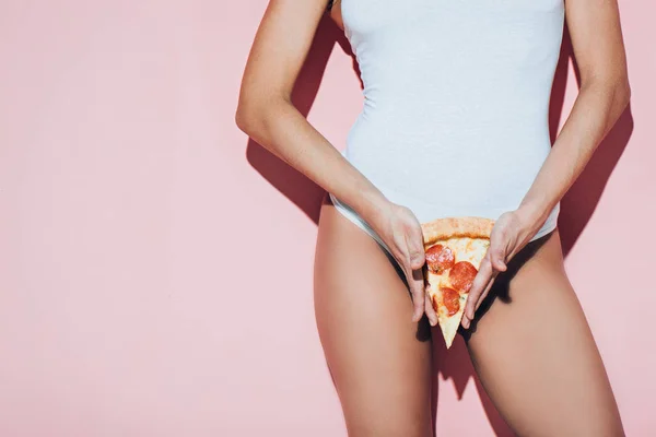 Partial view of woman in white bodysuit holding piece of italian pizza on pink background — Stock Photo