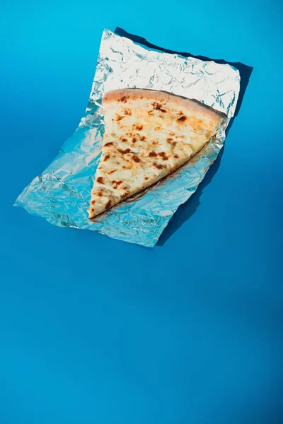 Close up view of piece of italian pizza on foil on blue background — Stock Photo
