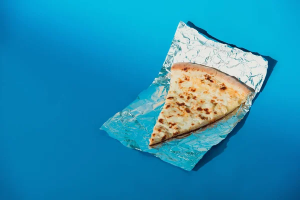 Close up view of piece of italian pizza on foil on blue background — Stock Photo