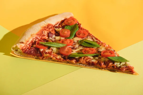Vista de cerca de pedazo de pizza con tomates cherry y albahaca sobre fondo colorido - foto de stock