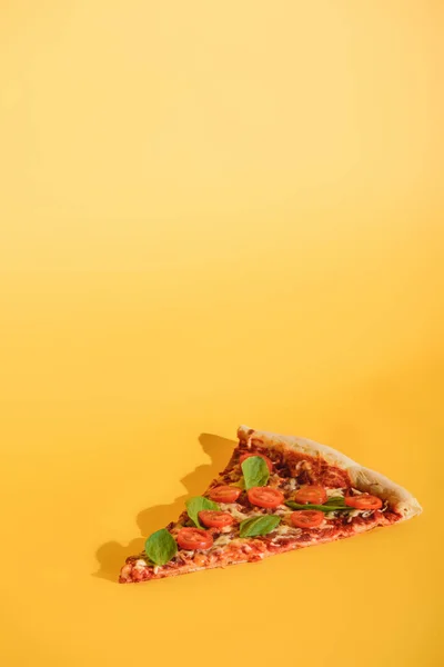 Close up view of piece of pizza with cherry tomatoes and basil on orange backdrop — Stock Photo