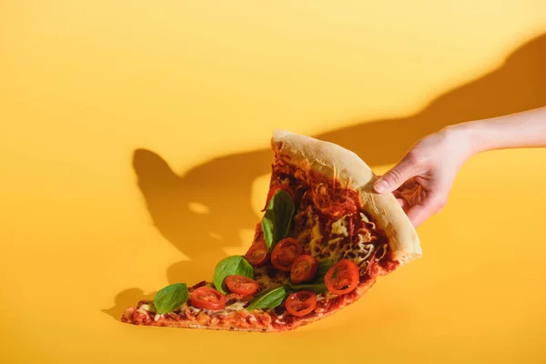 Partial view of woman holding piece of pizza with cherry tomatoes in hand on yellow background — Stock Photo