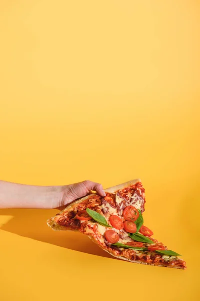 Partial view of woman holding piece of pizza with cherry tomatoes in hand on yellow background — Stock Photo