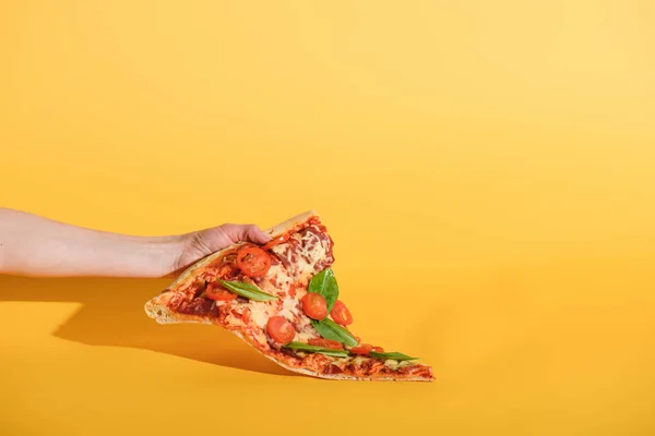 Partial view of woman holding piece of pizza with cherry tomatoes in hand on yellow background — Stock Photo