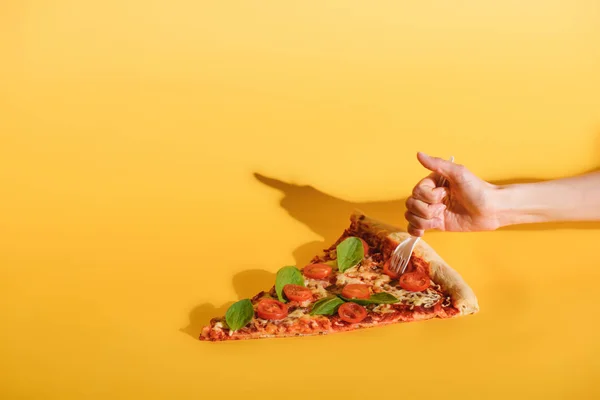 Partial view of woman sticking disposable fork into piece of pizza on yellow backdrop — Stock Photo