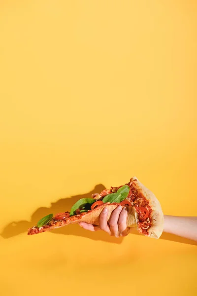 Partial view of woman holding piece of pizza in hand on yellow background — Stock Photo