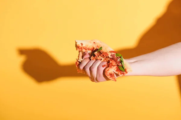 Partial view of woman squeezing piece of pizza in hand on yellow background — Stock Photo