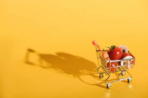 Close up view of little shopping cart with fresh ingredients for pizza on orange backdrop — Stock Photo