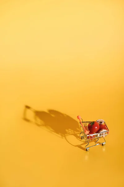 Vista de perto de pouco carrinho de compras com ingredientes frescos para pizza no fundo laranja — Fotografia de Stock