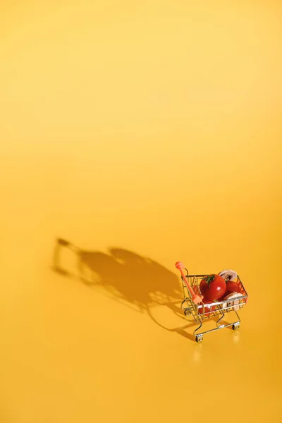 Vista de cerca del pequeño carrito de compras con ingredientes frescos para pizza sobre fondo naranja - foto de stock