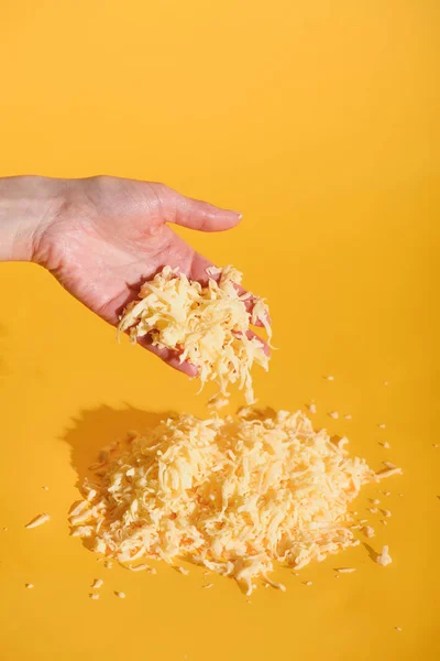 Colpo ritagliato di mano femminile con formaggio grattugiato su sfondo giallo — Foto stock