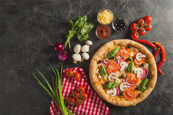 Flat lay with italian pizza and fresh ingredients on dark surface — Stock Photo