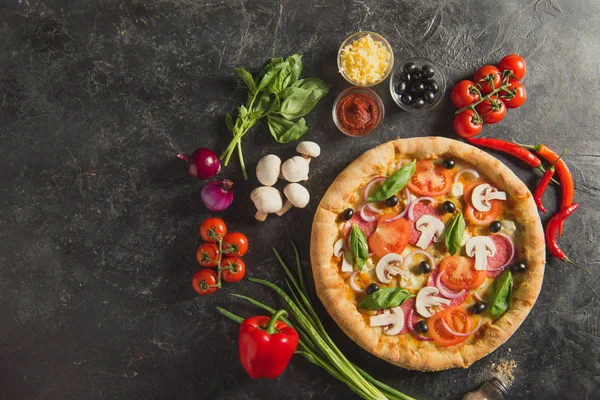 Flat lay with italian pizza and fresh ingredients on dark surface — Stock Photo