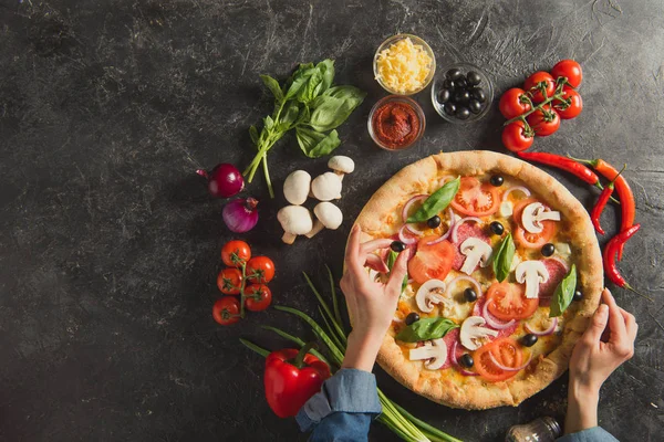 Cropped shot of woman putting black olives on italian pizza on dark tabletop — Stock Photo