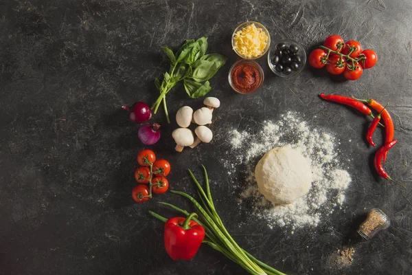 Flat lay with raw dough and fresh ingredients for pizza on dark surface — Stock Photo