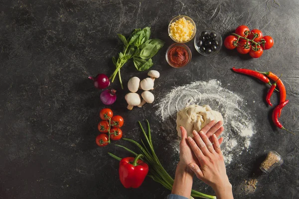 Cropped shot of woman braking dough while cooking italian pizza on dark tabletop — Stock Photo