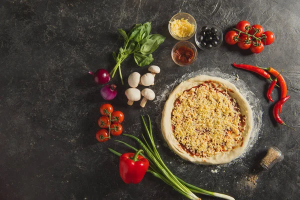 Vue de dessus de la pizza italienne crue et des ingrédients frais autour sur la surface sombre — Photo de stock