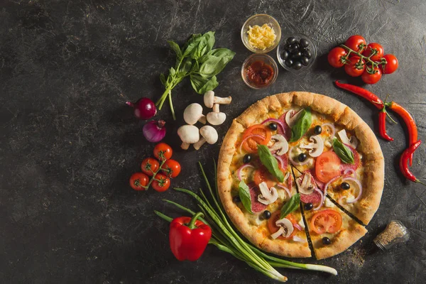 Flat lay with italian pizza and fresh ingredients on dark surface — Stock Photo