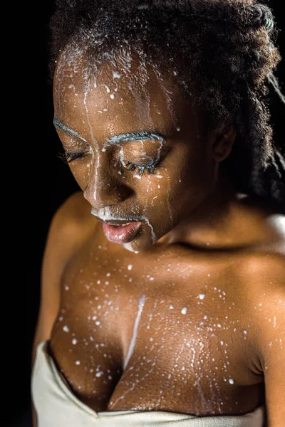 Belle jeune femme afro-américaine avec du lait renversé sur le visage isolé sur noir — Photo de stock
