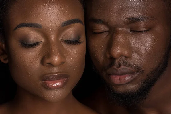 Jovem casal afro-americano com gotas de água em rostos posando com olhos fechados em preto — Fotografia de Stock